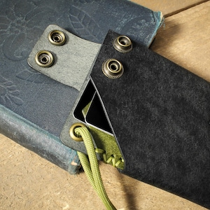 May include: A black leather wallet with a green stitching detail and a small leaf logo. The wallet is attached to a green cord and has a flap with three brass snaps.