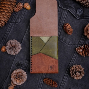 May include: A vertical leather card holder featuring a tri-color design with a light brown top section, an olive green middle pocket, and a dark brown bottom section. The wallet has black edge stitching and a small embossed leaf logo on the front.