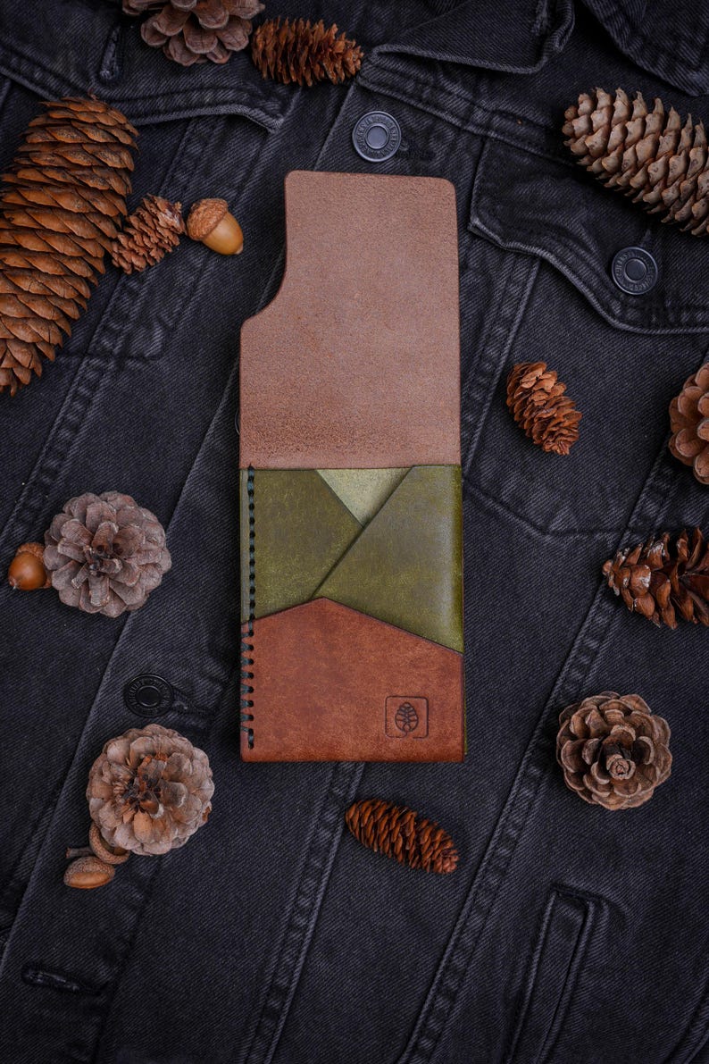 May include: A vertical leather card holder featuring a tri-color design with a light brown top section, an olive green middle pocket, and a dark brown bottom section. The wallet has black edge stitching and a small embossed leaf logo on the front.