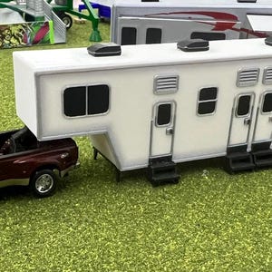 May include: A burgundy pickup truck towing a white fifth wheel camper. The camper has multiple windows and a door on each side.