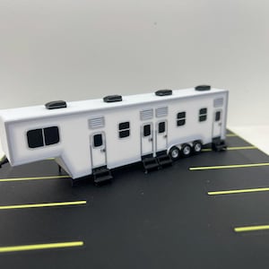 May include: A white model of a large, multi-room trailer with black accents and wheels. The trailer has multiple windows and doors.