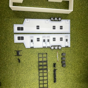 May include: A white model kit of a large semi-trailer truck with a flatbed trailer. The kit includes the cab, the trailer, and a ladder. The kit is made of plastic and is unassembled.