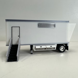 May include: White trailer with a door and a window, a set of stairs leading up to the door, and a single wheel visible on the right side.