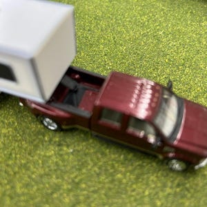 May include: A burgundy pickup truck towing a white camper trailer. The truck has a black bed and a black interior. The camper has a black window and a white roof.