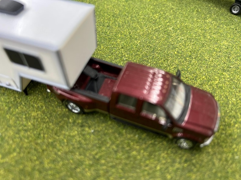 May include: A burgundy pickup truck towing a white camper trailer. The truck has a black bed and a black interior. The camper has a black window and a white roof.