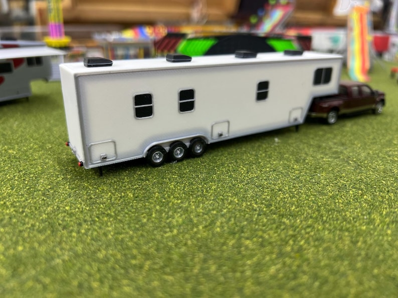 May include: White toy trailer with black accents and three windows. The trailer is attached to a smaller, dark red toy truck.