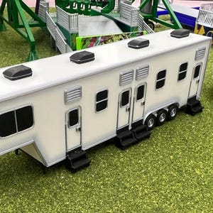 May include: A white trailer with multiple doors and windows. The trailer has a white roof with multiple black vents. The trailer is sitting on a green grassy surface.