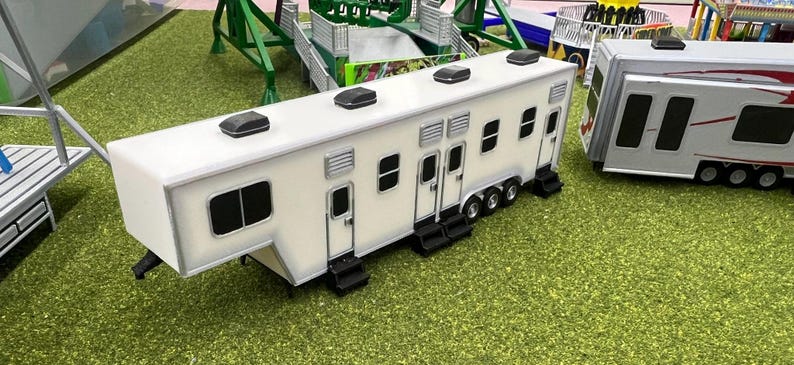 May include: A white trailer with multiple doors and windows. The trailer has a white roof with multiple black vents. The trailer is sitting on a green grassy surface.