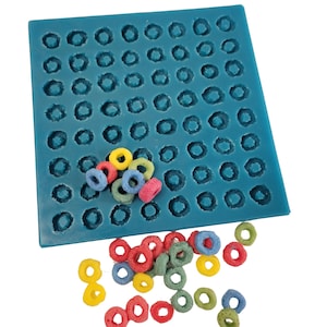 May include: A teal silicone mold with numerous circular indentations, alongside a scattering of colorful, ring-shaped cereal pieces. The cereal pieces are in various colors, including yellow, red, green, and blue. The mold is square and sits on a white background.