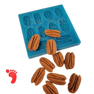 May include: Blue silicone mold with 10 pecan nut shapes. The mold is labeled "Red Foot Craft Supply". There are 10 pecan nuts scattered around the mold.