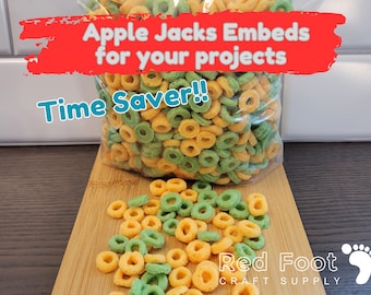 May include: A bag of green and orange cereal rings called Apple Jacks Embeds for your projects. The bag is on a wooden surface with a few cereal rings scattered around it. The text "Time Saver!!" is written in white letters on a red background. The text "Red Foot Craft Supply" is written in white letters on a red background with a red footprint.