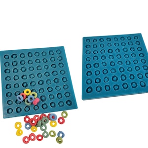 May include: Two teal silicone molds with circular indentations, alongside colorful cereal pieces. The molds are rectangular and designed for creating small, round shapes. The cereal pieces are in various colors, including yellow, red, and green.