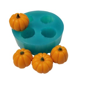 May include: A teal silicone mold with four pumpkin-shaped cavities, accompanied by four small, orange pumpkin figurines. The pumpkins have detailed ridges and green stems, perfect for crafting seasonal decorations or treats.