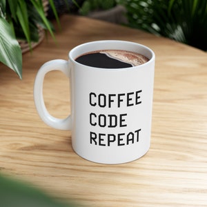 May include: White coffee mug with black text that reads "COFFEE CODE REPEAT".