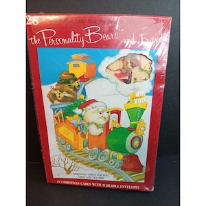 May include: A package of 29 Christmas cards featuring the Personality Bears and Friends. The cards feature a train with bears and a Christmas tree. The package includes a bonus card for teachers. The text on the package reads "Christmas Cards for Boys, Girls and Teacher" and "29 Christmas Cards with Mailable Envelopes".