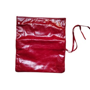 May include: A bright red, rectangular clutch bag with a glossy finish. The bag has a simple design with a fold-over flap and a long, thin strap for carrying or tying. The material appears to be leather or a leather-like material.