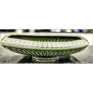 May include: A green ceramic decorative bowl with a rectangular shape and a pedestal base. The bowl has a detailed, repeating pattern around the rim and base. The bowl is approximately 12 inches long.