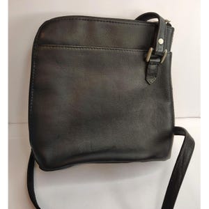 Puede incluir: Un bolso bandolera de cuero negro con una hebilla plateada y un cierre de cremallera. El bolso tiene una correa larga ajustable.