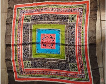 Può includere: Foulard quadrato in seta con un design geometrico. La sciarpa presenta un bordo marrone, con una serie di quadrati colorati in arancione, verde, blu e marrone. Il quadrato centrale è blu con accenti floreali rosa. Un accessorio vintage.