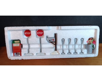 Puede incluir: Un conjunto de señales de tráfico en miniatura y accesorios para maquetas de trenes o dioramas. El conjunto incluye dos señales de stop rojas, un buzón, una farola y un cubo de basura.