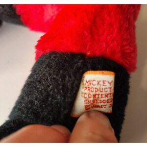 May include: Close-up of a vintage plush toy with black and red fur. A white tag with the text "MICKEY PRODUCT CONTENTS SHREDDED &copy; WALT D" is attached to the toy. The toy appears to be a collectible item.