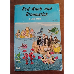 May include: Vintage paperback book titled "Bed-Knob and Broomstick" by Mary Norton. The cover features a blue background with illustrations of cartoon characters, fish, and people. The book has a worn appearance.