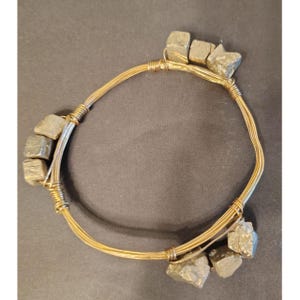 Peut inclure: Un collier fait à la main avec des pierres de pyrite brutes et du fil doré. Les pierres de pyrite sont de forme irrégulière et ont une couleur gris-or métallique. Le fil est enroulé autour des pierres et forme la forme circulaire du collier.