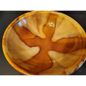 Könnte beinhalten: Eine Keramikschale mit glänzendem Finish. Die Schale hat ein einzigartiges Muster aus braunen und cremefarbenen Farben, das einen auffälligen visuellen Effekt erzeugt. Der Innenraum hat eine glatte Oberfläche, während die Außenseite sich leicht strukturiert anfühlt. Die Schale ist ideal zum Servieren von Speisen.