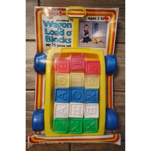 May include: A vintage Unlold preschool toy set, "Wagon Load o' Blocks." The yellow wagon holds 16 colorful alphabet blocks. The packaging is yellow, red, and white, with blue wheels. The set is for ages 2 and up.