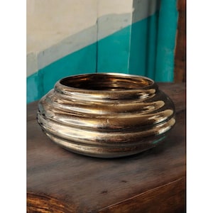 May include: A gold-toned metal bowl with a rounded, fluted design. The bowl has a smooth, reflective surface.
