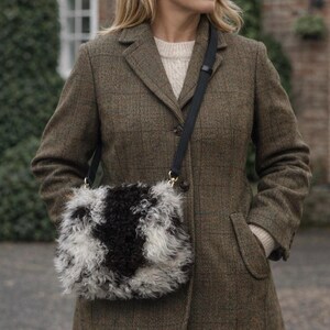 May include: A crossbody bag with a fluffy, textured design in black and white. The bag has a black strap and gold-colored hardware. The bag is worn over a brown tweed coat.