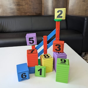 May include: A colorful tower of blocks with numbers 1 through 9. The blocks are stacked in a pyramid shape, with the tallest block being number 9. The blocks are made of plastic and have a smooth, glossy finish.