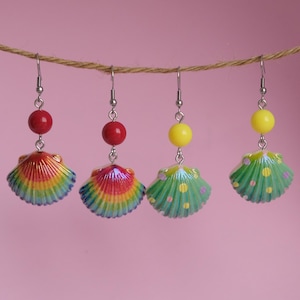 May include: Three pairs of colourful shell earrings with a rainbow, green, and green with white polka dots design. Each earring has a silver hook and a bead in red, yellow, or yellow.