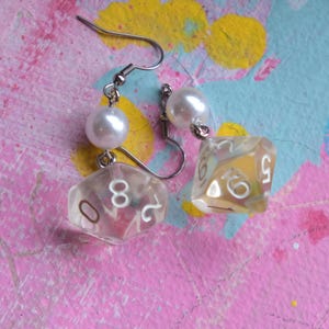 May include: A pair of silver dangle earrings with a clear iridescent dice charm and a white pearl bead on each earring.