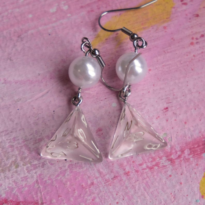 May include: A pair of silver dangle earrings with a clear, triangular, four-sided dice charm and a white pearl bead on each earring.