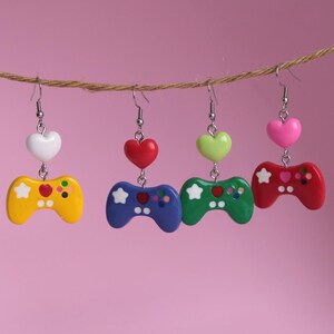 Puede incluir: Cuatro pares de pendientes colgantes con un dije de mando de videojuego colorido y un dije de corazón. Los corazones son blanco, rojo, verde y rosa. Los mandos son amarillo, azul, verde y rojo.