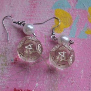 May include: A pair of silver dangle earrings with clear plastic dice charms and white pearl accents.