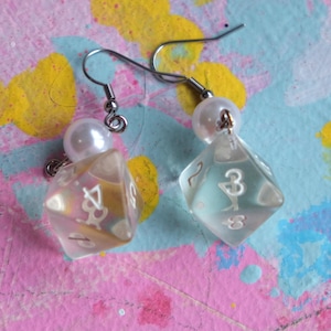 May include: A pair of silver dangle earrings with a white pearl charm and a clear iridescent dice charm. The dice charms have white numbers on them.
