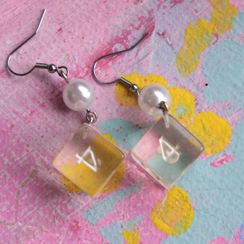 May include: A pair of silver earrings with clear plastic dice charms and white pearl accents.