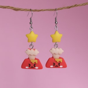 May include: A pair of red and yellow volcano earrings with a white cloud and a yellow star on top. The volcano has a grumpy face.