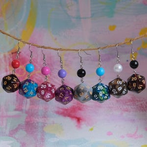 May include: A set of eight dangle earrings featuring a variety of colours and designs. Each earring features a 20-sided die with gold numbers and a small bead in a coordinating colour.