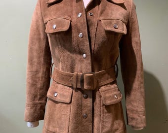 May include: A brown suede jacket with a belted waist, long sleeves, and multiple pockets. The jacket has a button-up front closure and a collared neckline.
