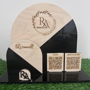 Pode incluir: Uma placa de madeira com um design preto e branco. A placa apresenta o texto "RA Kreations Custom Gifts and Decor" e "let's connect". Existem dois códigos QR na placa, um para Etsy e outro para Instagram.