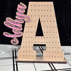 May include: A wooden letter A with a polka dot pattern, standing on a base. The letter is decorated with the word "Olivia" in pink cursive.