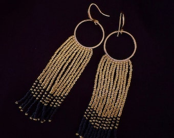 May include: A pair of gold and black beaded earrings with a hoop design. The earrings have a long, dangling fringe of beads.