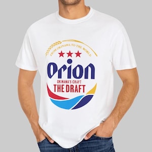 May include: White t-shirt featuring the Orion beer logo. The logo includes the word "Orion" in blue, three red stars, and the text "Okinawa's Craft The Draft". The shirt also has the text "From Okinawa to the World".