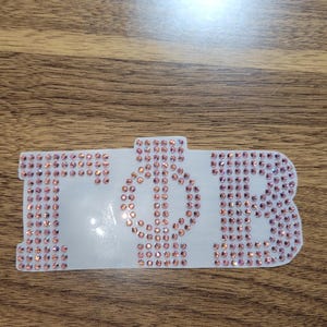 May include: A white background with the letters "ZPB" in pink rhinestones.