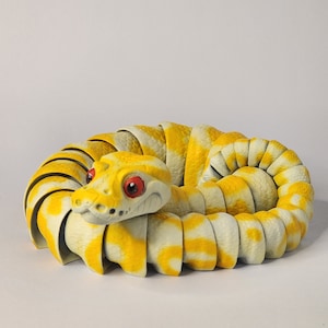 May include: A yellow and white segmented snake figurine with red eyes. The snake is curled up in a coil.