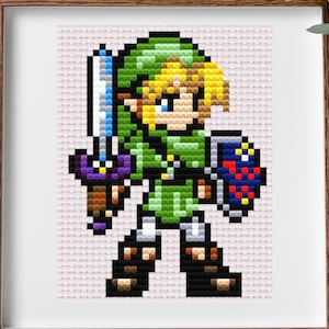 Könnte beinhalten: Ein Kreuzstichmuster von Link aus der Videospielserie The Legend of Zelda. Das Muster zeigt Link in seiner grünen Tunika, mit einem Schwert und einem Schild. Der Hintergrund ist hellrosa.