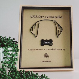 May include: A framed pet memorial with a dog ear outline and a bone-shaped tag reading "Sandy." The text "With love we remember" and "A loyal friend, a cherished memory" are displayed. The frame includes the years 2010-2025.